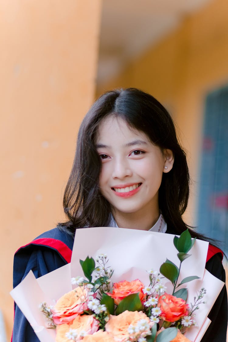 Portrait Of Smiling Girl In Graduation Gown With Flowers