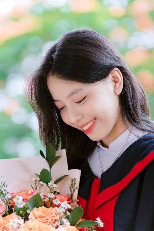 Young Woman in Blue and Red Graduation Gown Holding a Flower Bouquet