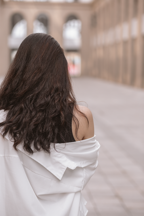 Free Back view of a woman with long hair and white blouse walking outdoors in Hanoi, Vietnam. Stock Photo