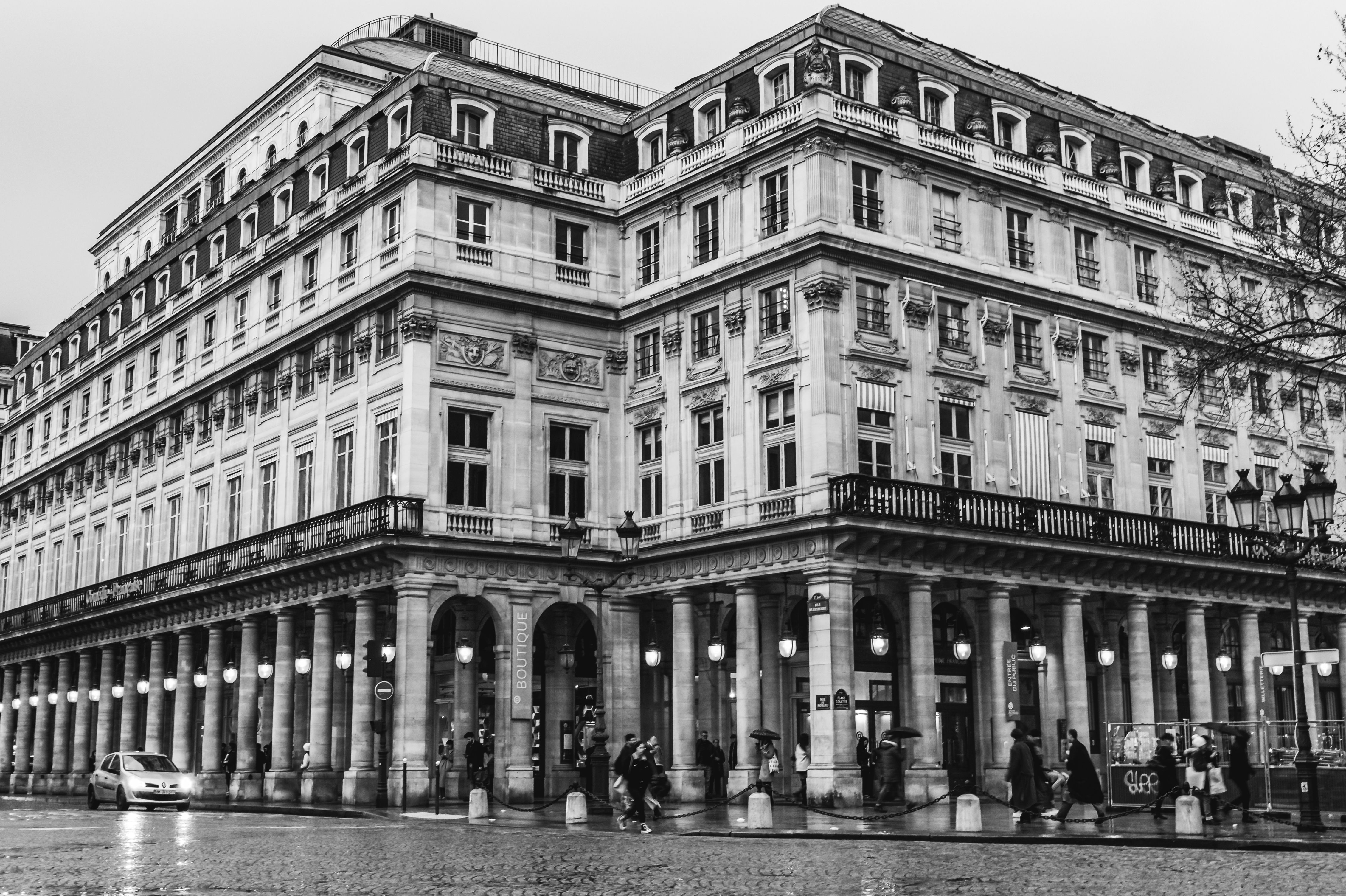 Black and white photo of a classic Parisian building with columns and pedestrians.