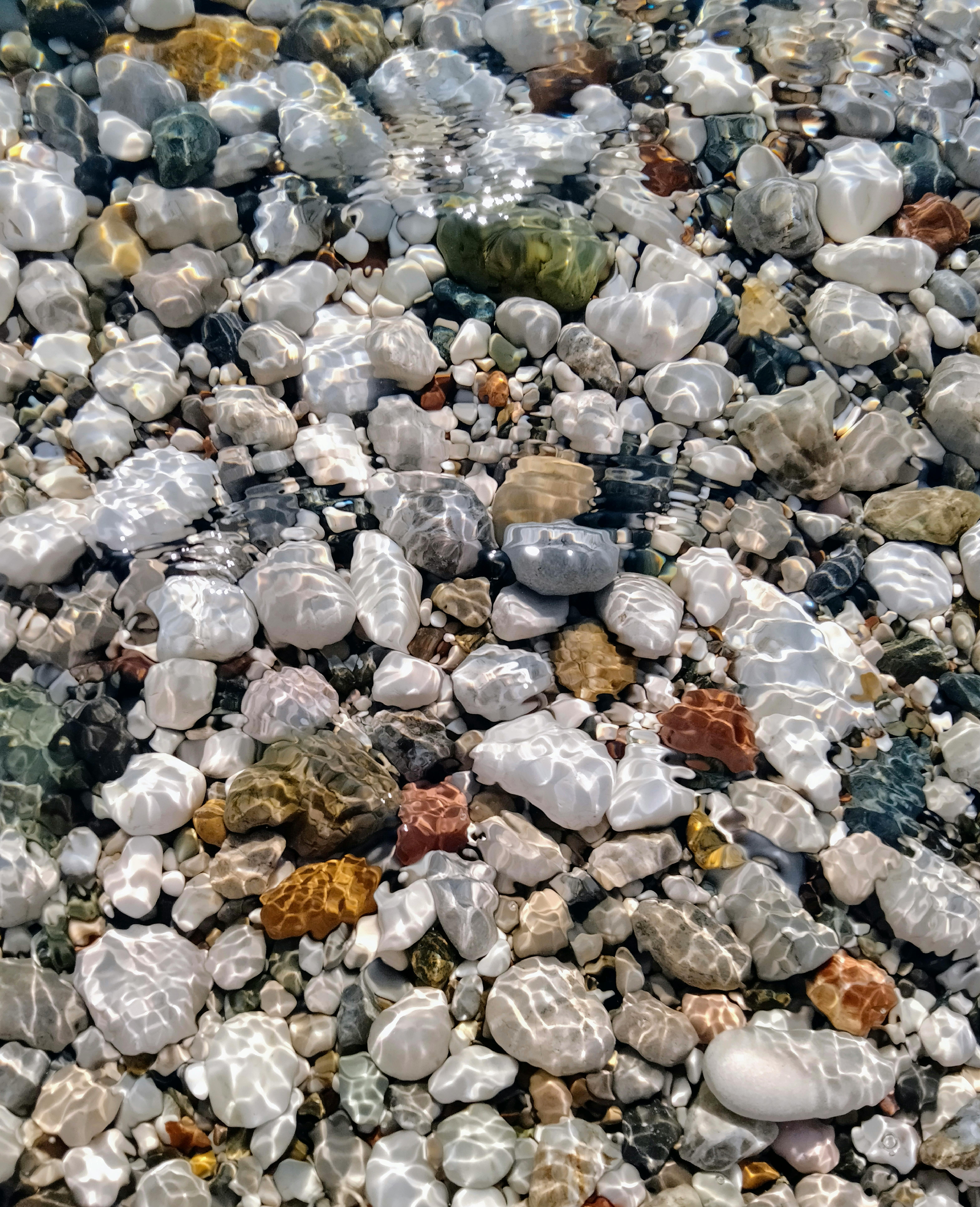 Top view of various pebbles submerged in clear water with sunlight reflections.