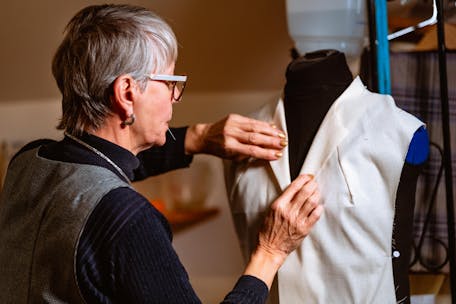 Senior woman sewing a white garment on a mannequin in a tailor shop.