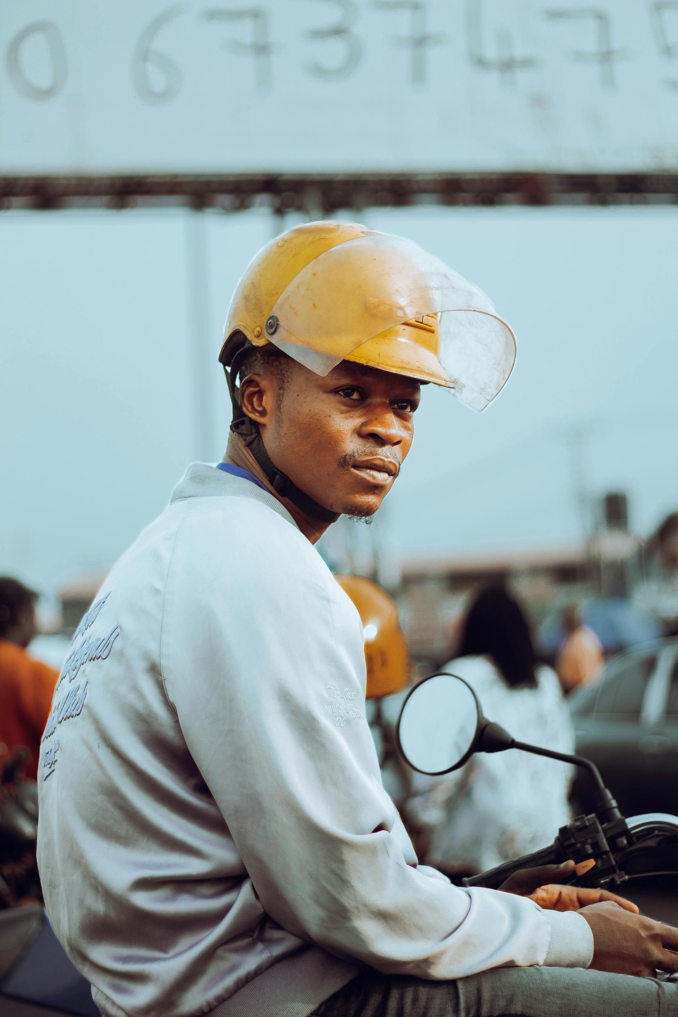 Portrait of a young man wearing a helmet on a motorcycle, outdoors with blurred urban background.