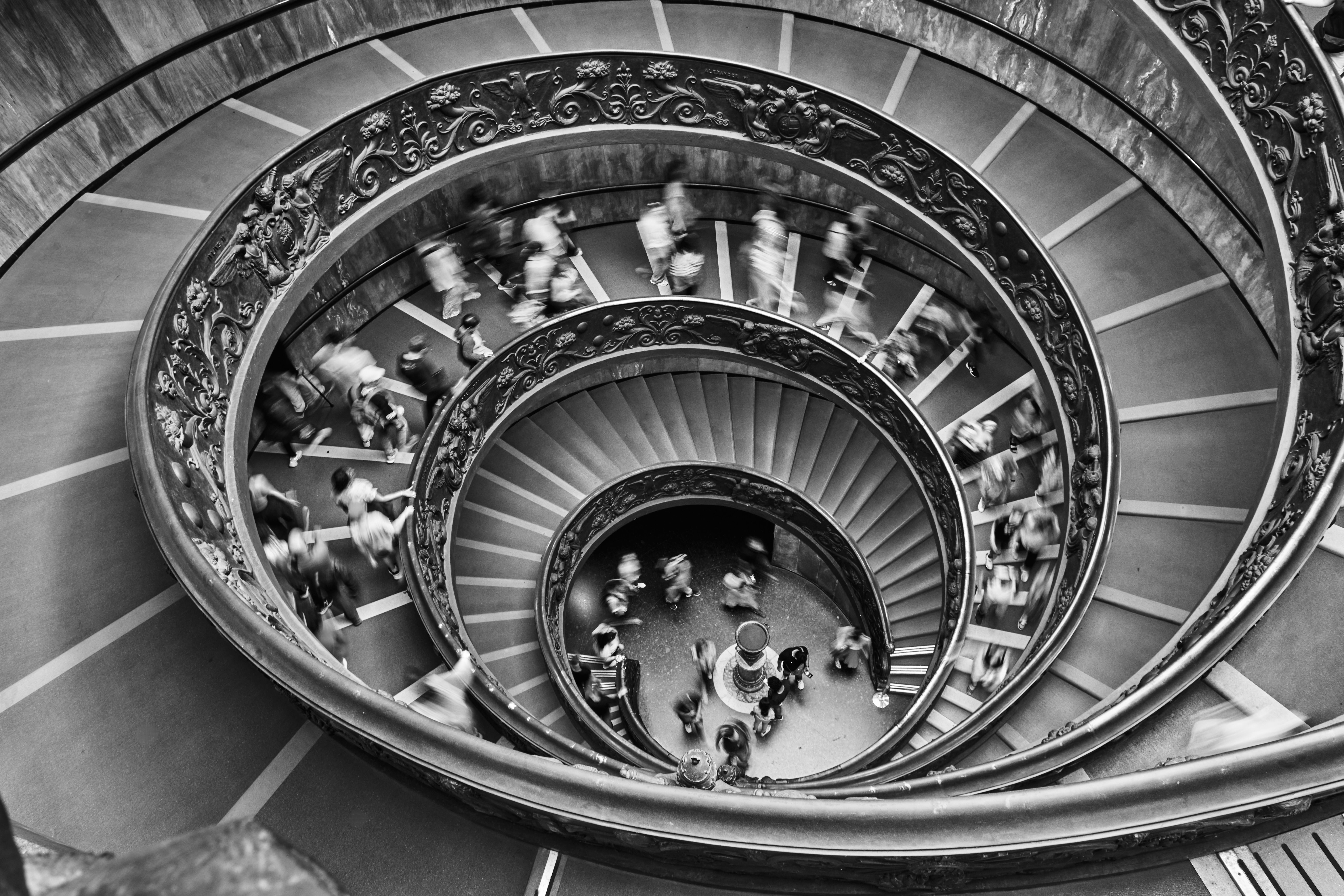 Black and white spiral staircase with motion blur of people at the Vatican Museum.