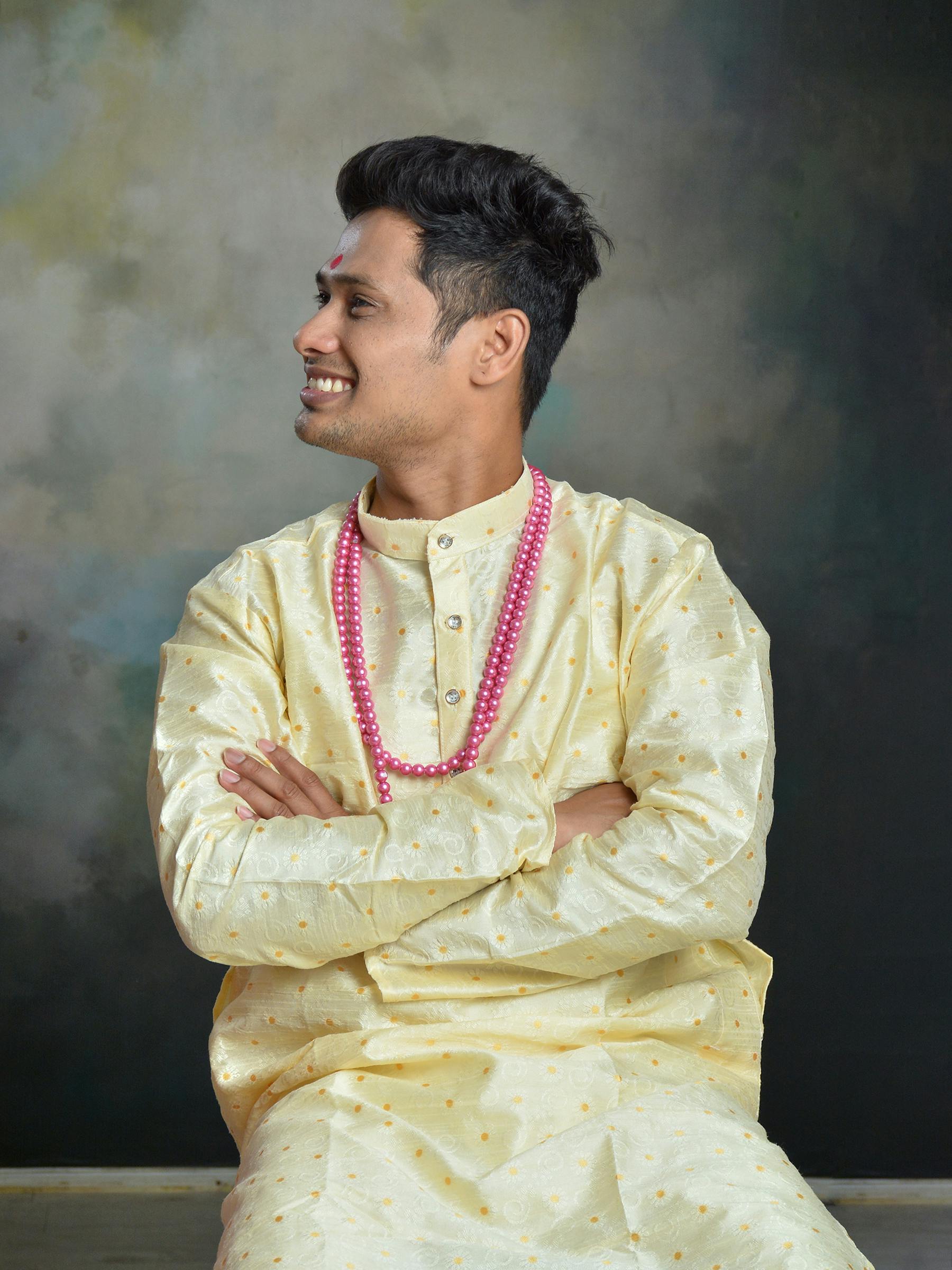 Portrait of a smiling man in traditional Indian clothing with a necklace, arms crossed.