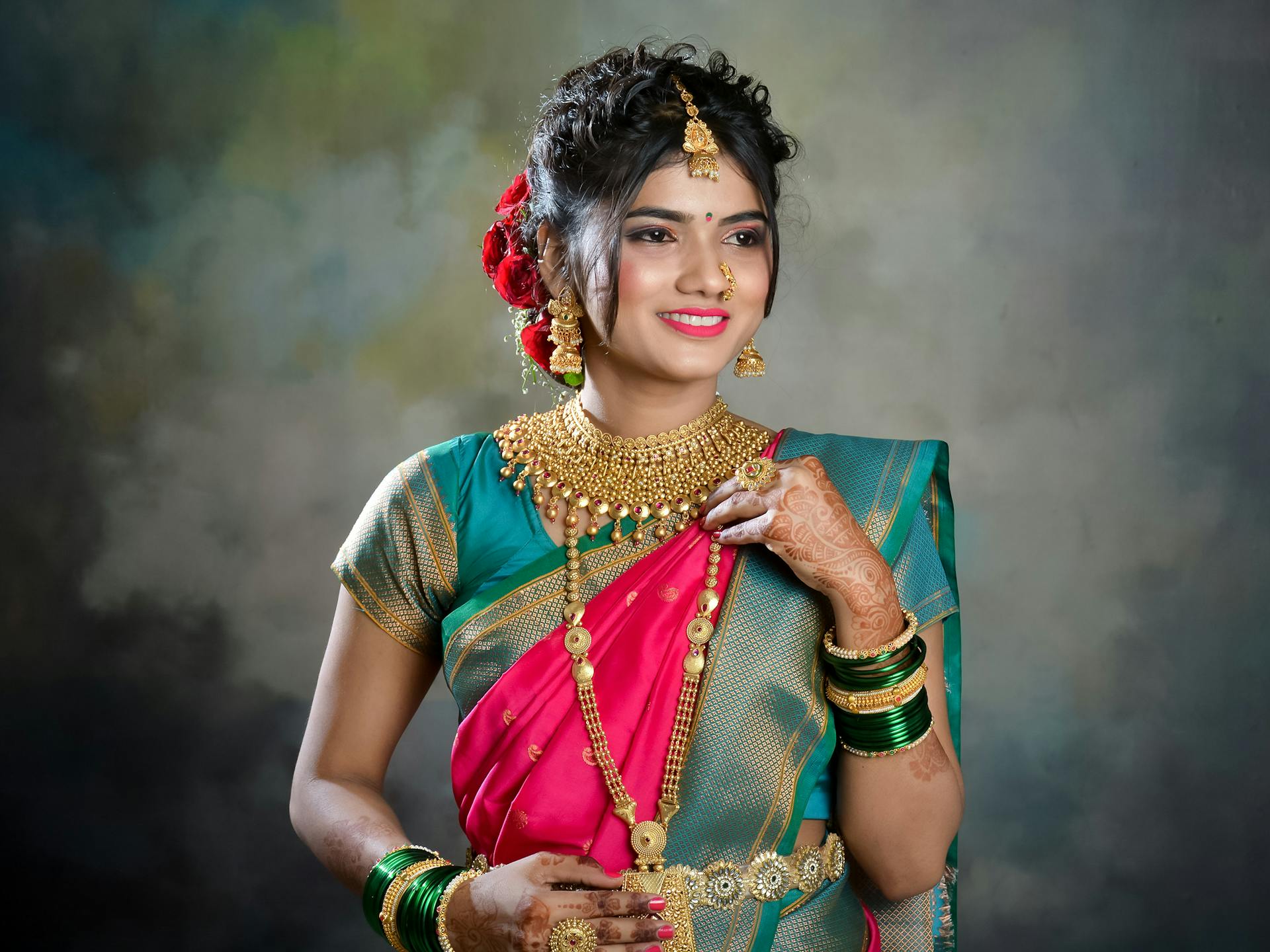 A young Indian bride smiling in colorful traditional attire and jewelry.