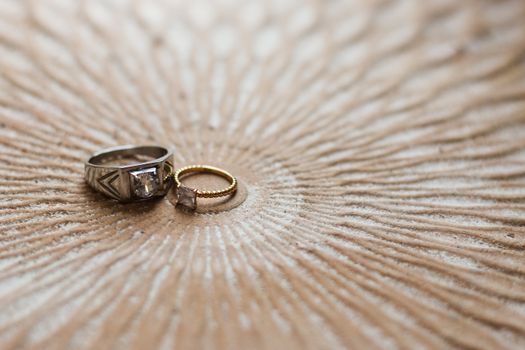 Close-up of elegant silver and gold rings on a textured circular surface, showcasing luxury and craftsmanship.