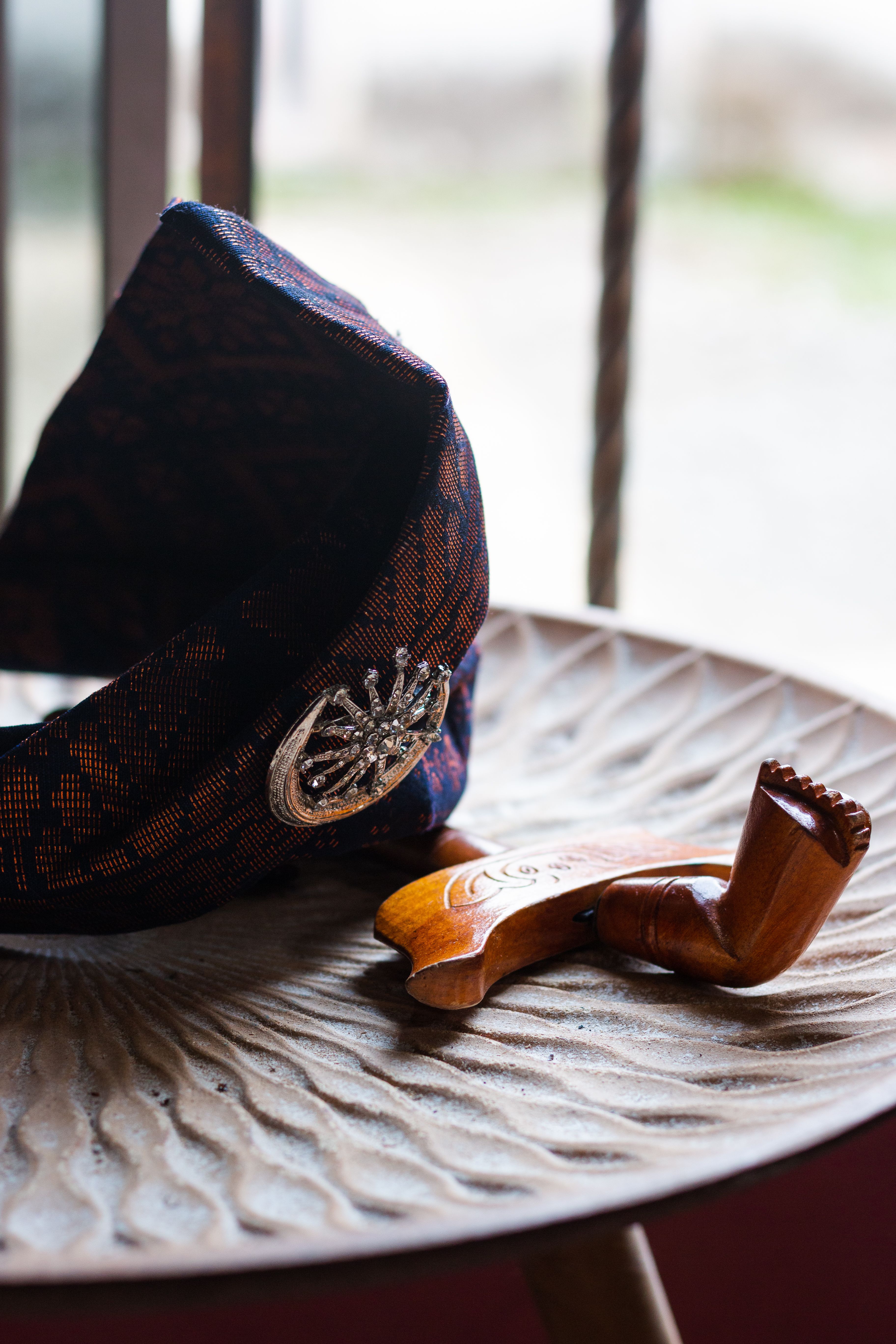 A unique wooden pipe and intricately patterned hat rest on a textured table, showcasing tradition and craftsmanship.