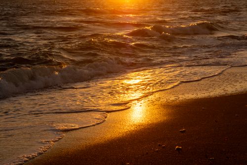 Free Waves gently lap the golden sand under a vibrant sunset, creating a serene coastal scene. Stock Photo