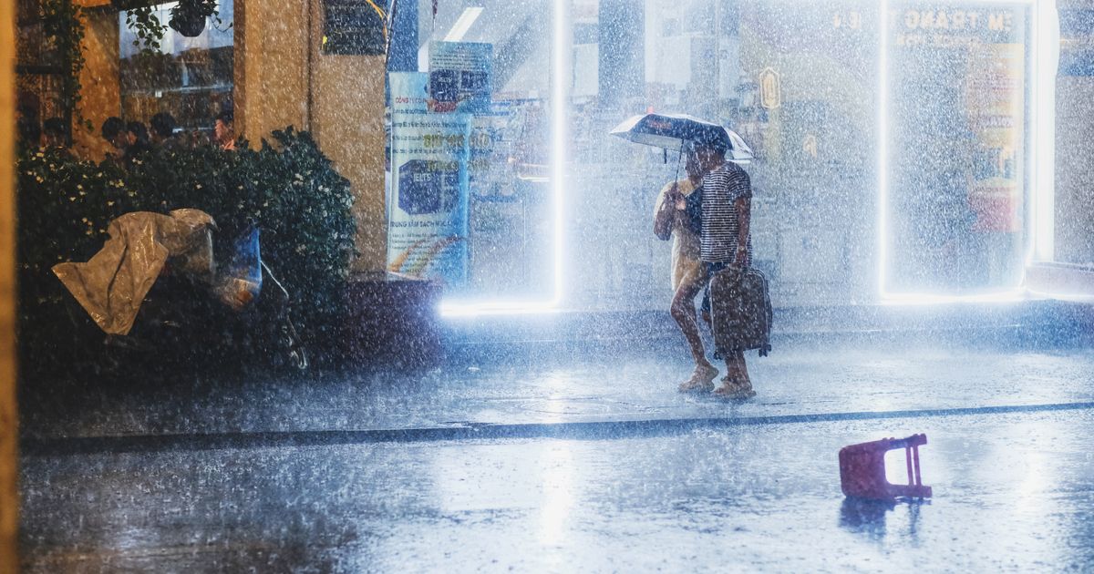 夜の街で、激しい雨の中を傘をさして歩く人
