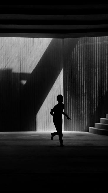 A boy's silhouette running against architectural shadows, creating dynamic urban scene.