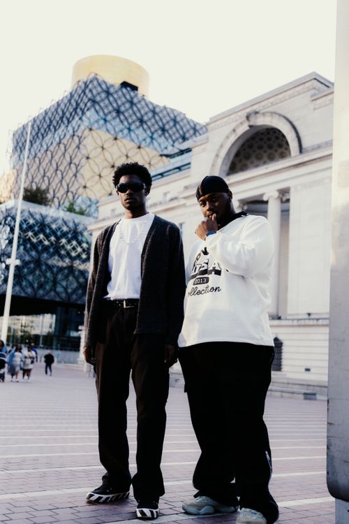 Free Two men posing in front of Birmingham's Library with modern architecture backdrop. Stock Photo