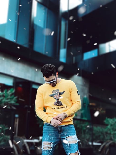 Stylish man in urban streetwear posing outdoors wearing a vibrant yellow sweater.