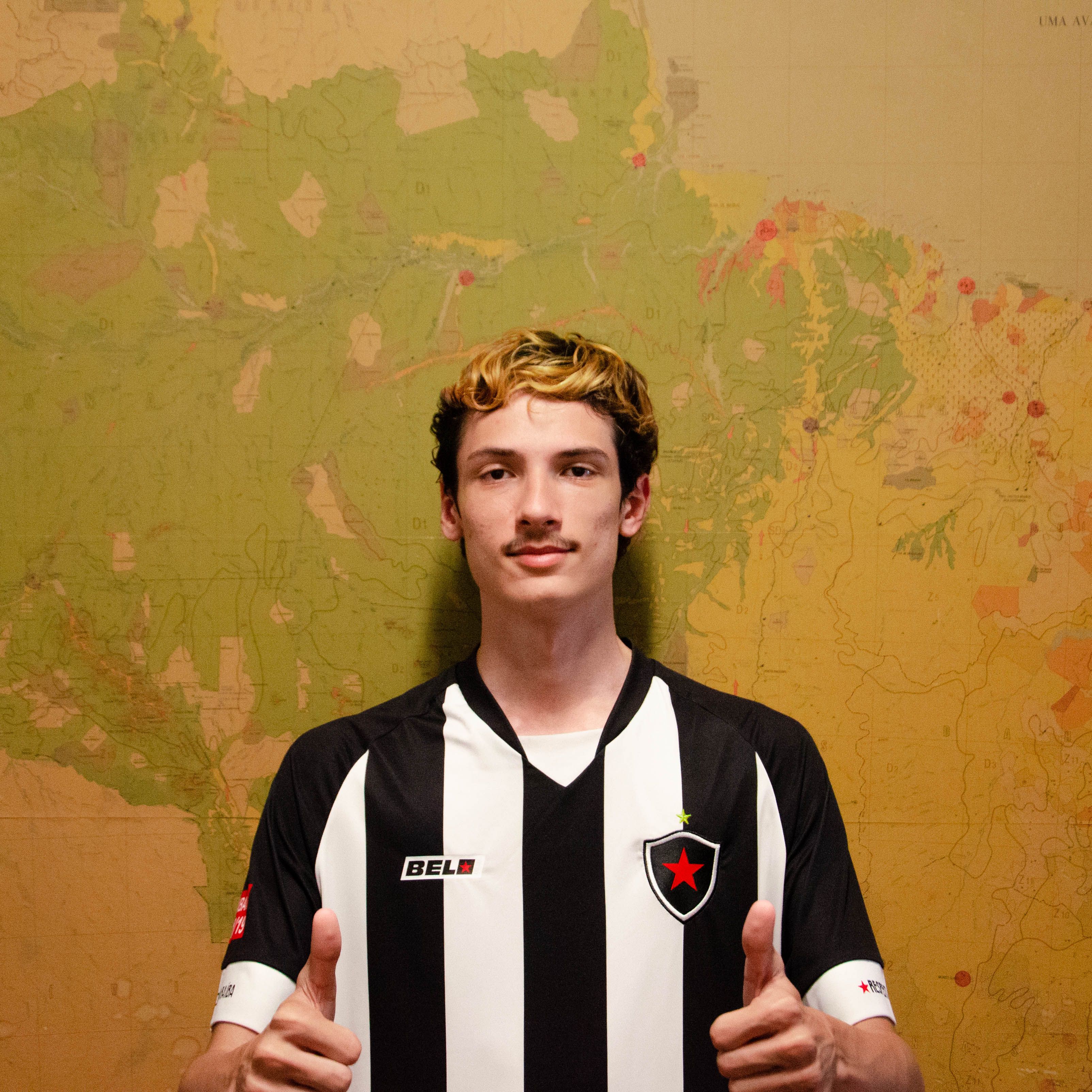 A young man in a black and white striped jersey gives thumbs up in front of a map background.