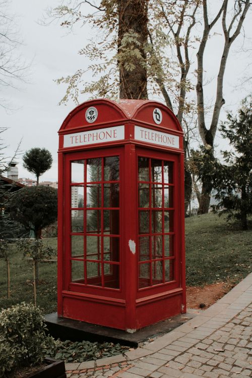 Free Vintage red telephone booth situated in a lush park in Trabzon, Türkiye. Stock Photo