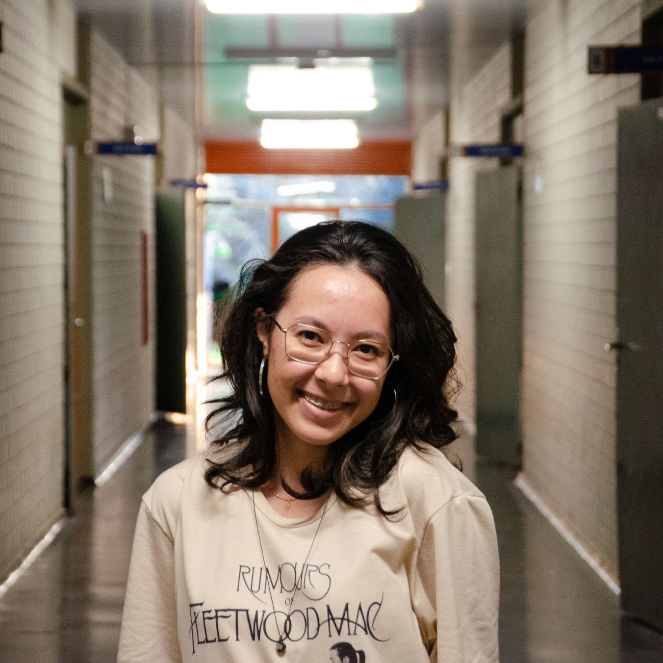 Cheerful woman with eyeglasses smiling in a brightly lit corridor.