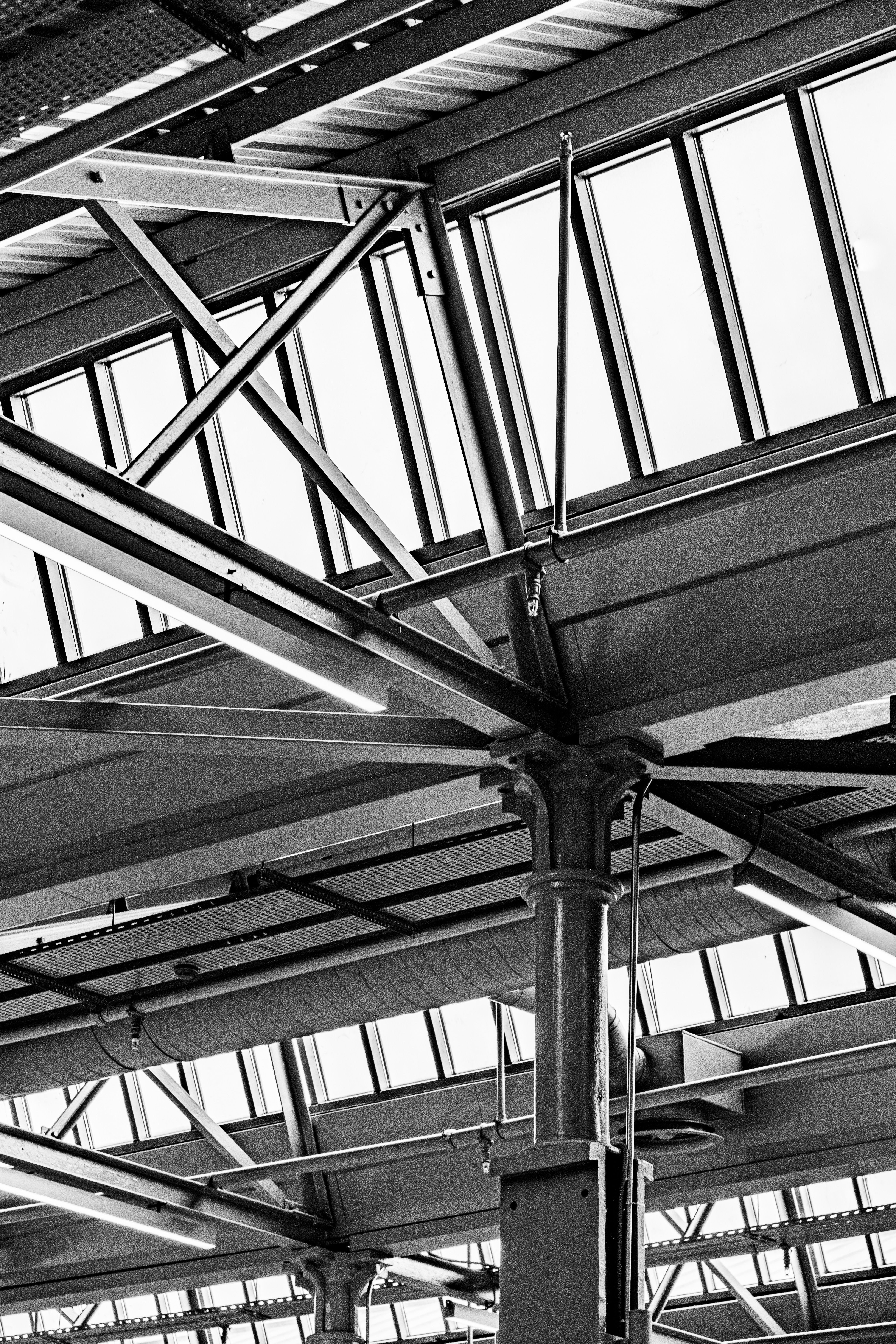 Black and white photo of a modern metal roof structure with glass panels in an industrial setting.