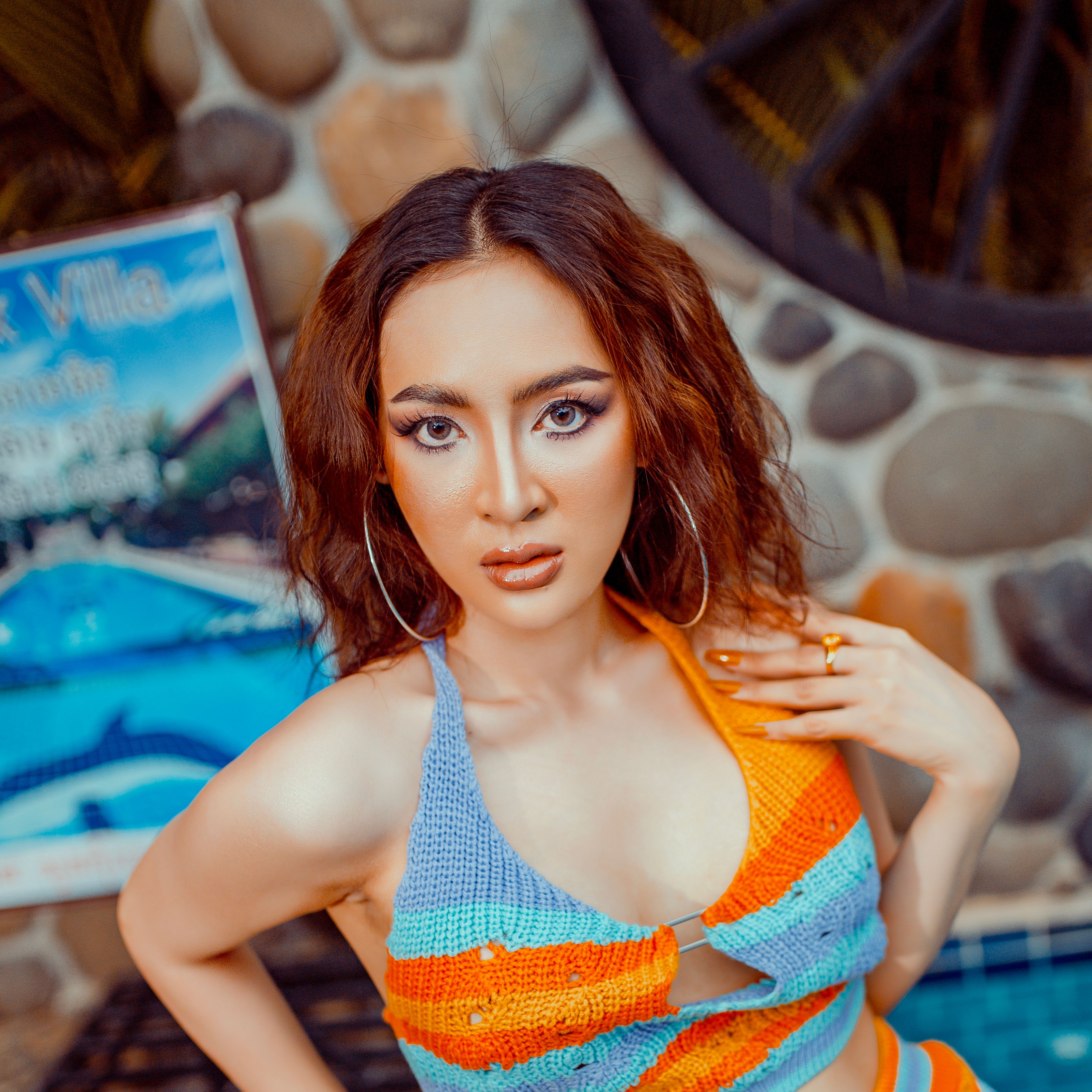Stylish woman posing outdoors in a vibrant knitted top with a rustic stone backdrop.