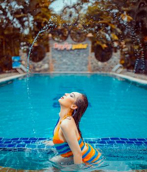 A woman in a colorful swimsuit posing dramatically in a pool, splashing water around her.