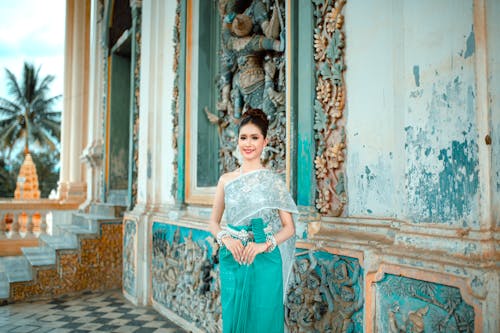 Smiling Woman in Traditional Clothing Standing by Temple Wall