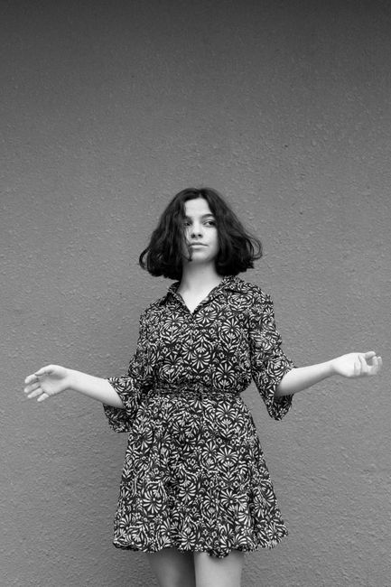 Black and white portrait of a woman in a patterned dress posing against a gray backdrop.