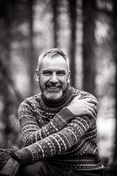 Free Black and white portrait of a smiling mature man with folded arms in a forest setting. Stock Photo