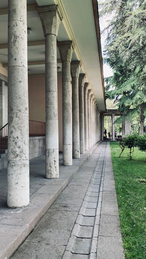 Free Discover serenity along a stone column walkway beside a lush green garden. A perfect blend of architecture and nature. Stock Photo