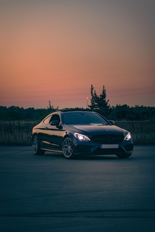Free Elegant black car with headlights on during dusk, set against a serene outdoor landscape. Stock Photo