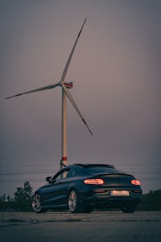 Elegant car parked near a towering wind turbine at dusk, symbolizing renewable energy.