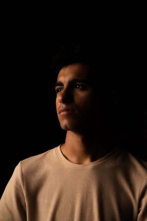 Free A contemplative young man gazing into the distance under dramatic studio lighting. Stock Photo