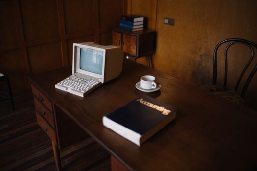 A nostalgic look at a vintage office with a retro computer, book, and cup on a wooden desk.