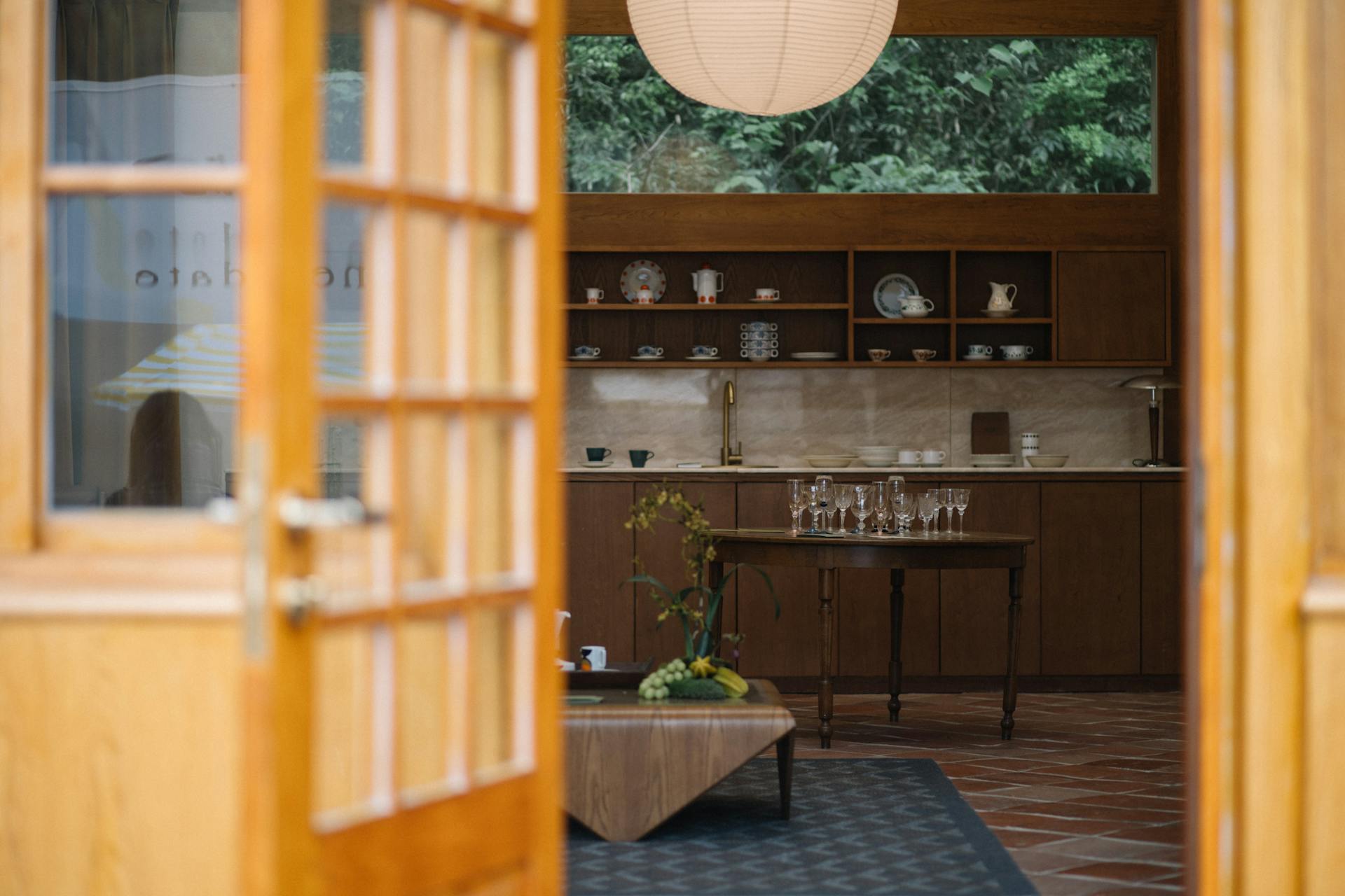 Inviting mid-century modern kitchen with wooden cabinetry and glassware, viewed through open doorway.