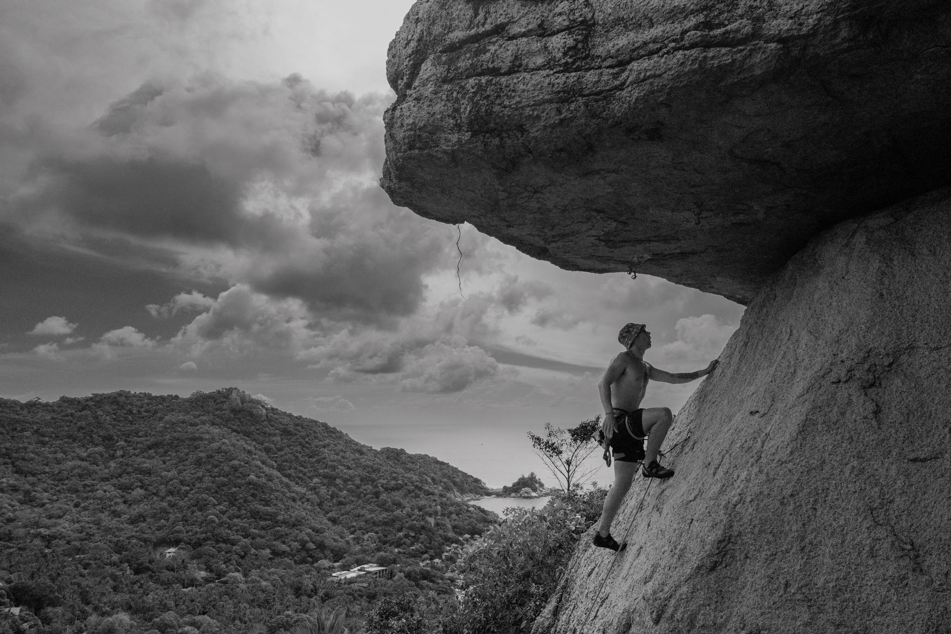 A man skillfully climbs a rock under a dramatic sky in a mountainous landscape.