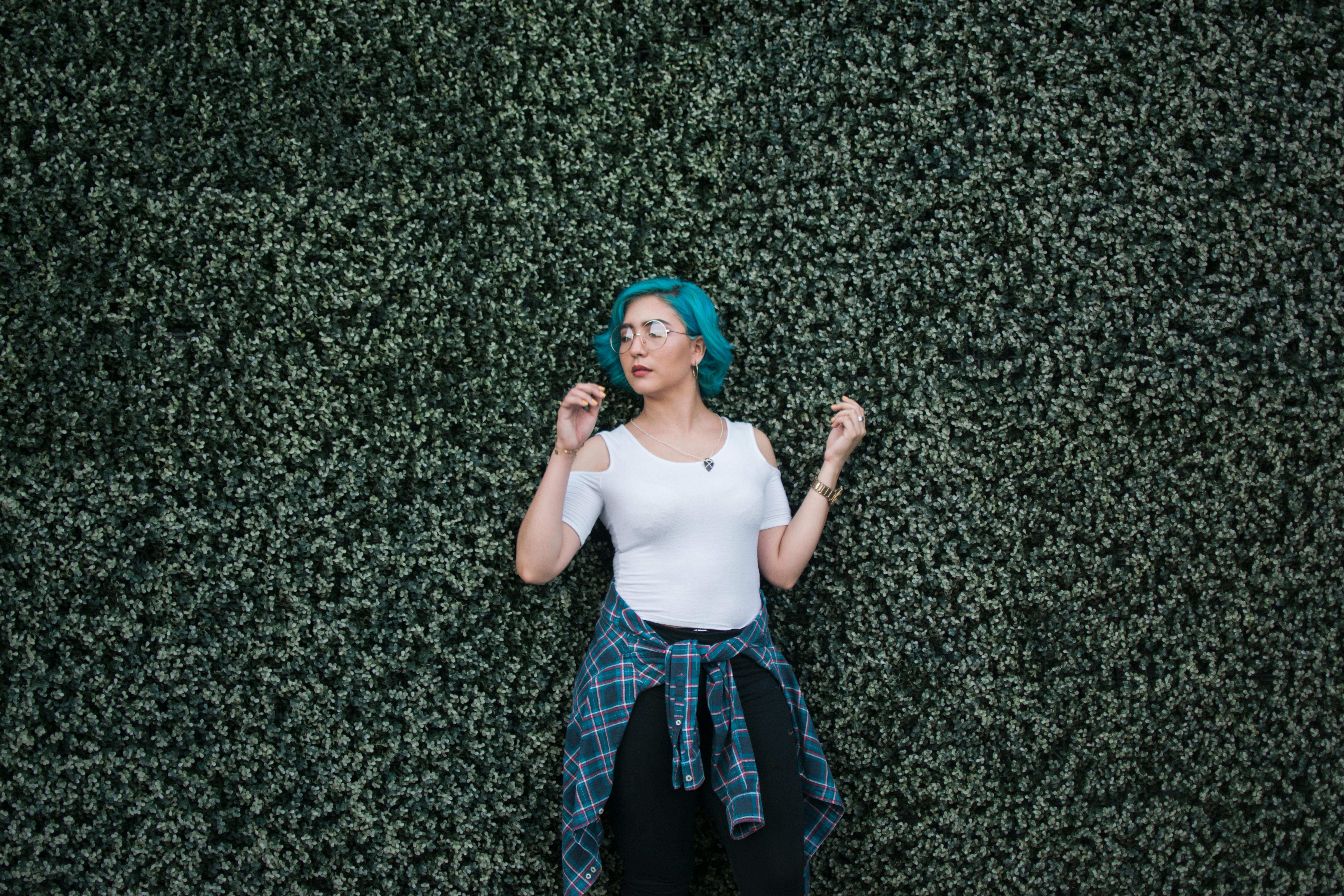 一位蓝发时尚女性自信地倚靠在户外绿叶绿墙上摆姿势