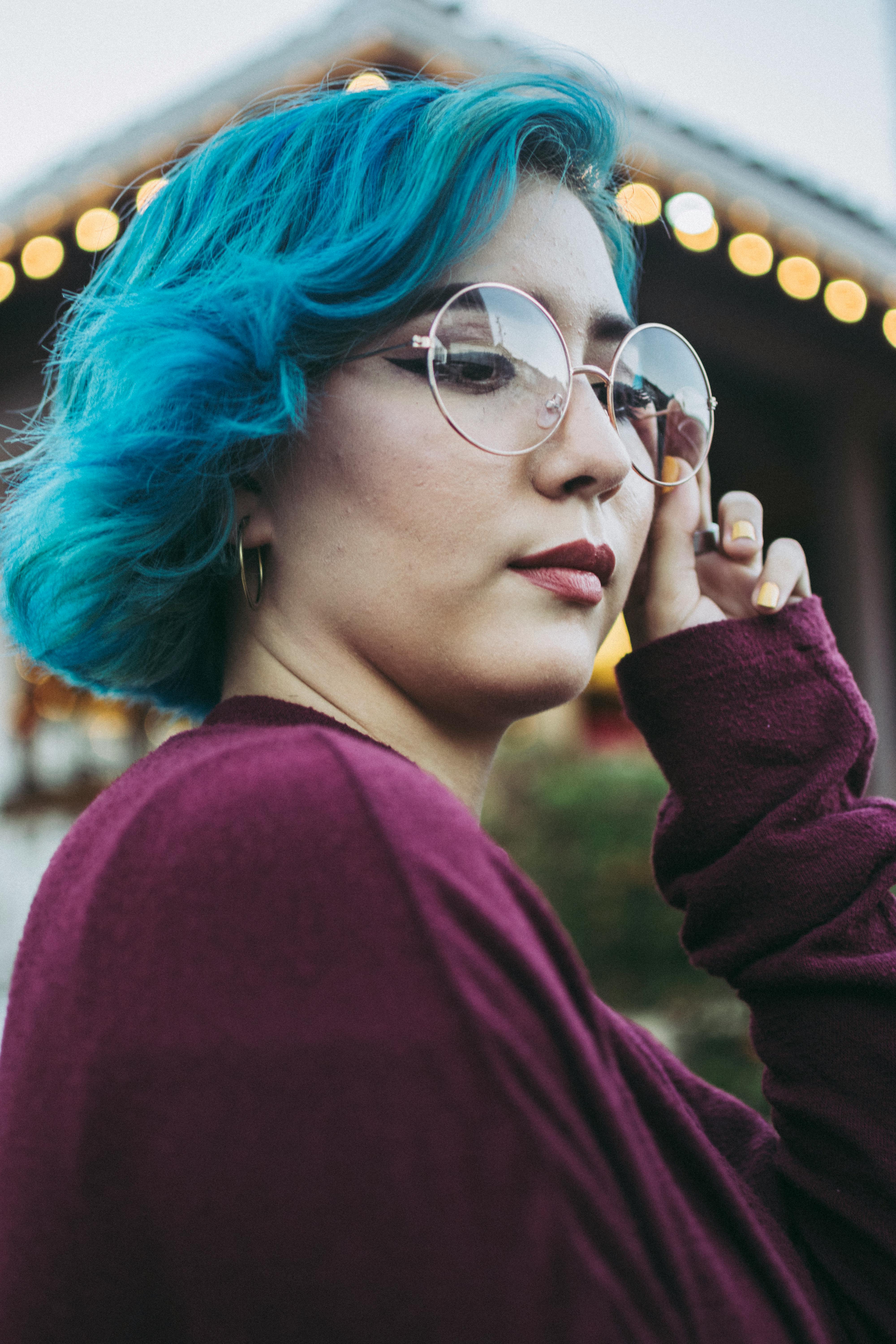 一位蓝发戴眼镜的时尚女性，在户外环境中散发着现代气息