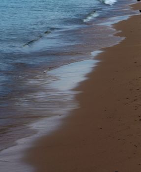 A peaceful sandy beach scene with gentle waves lapping the shore under a clear sky.