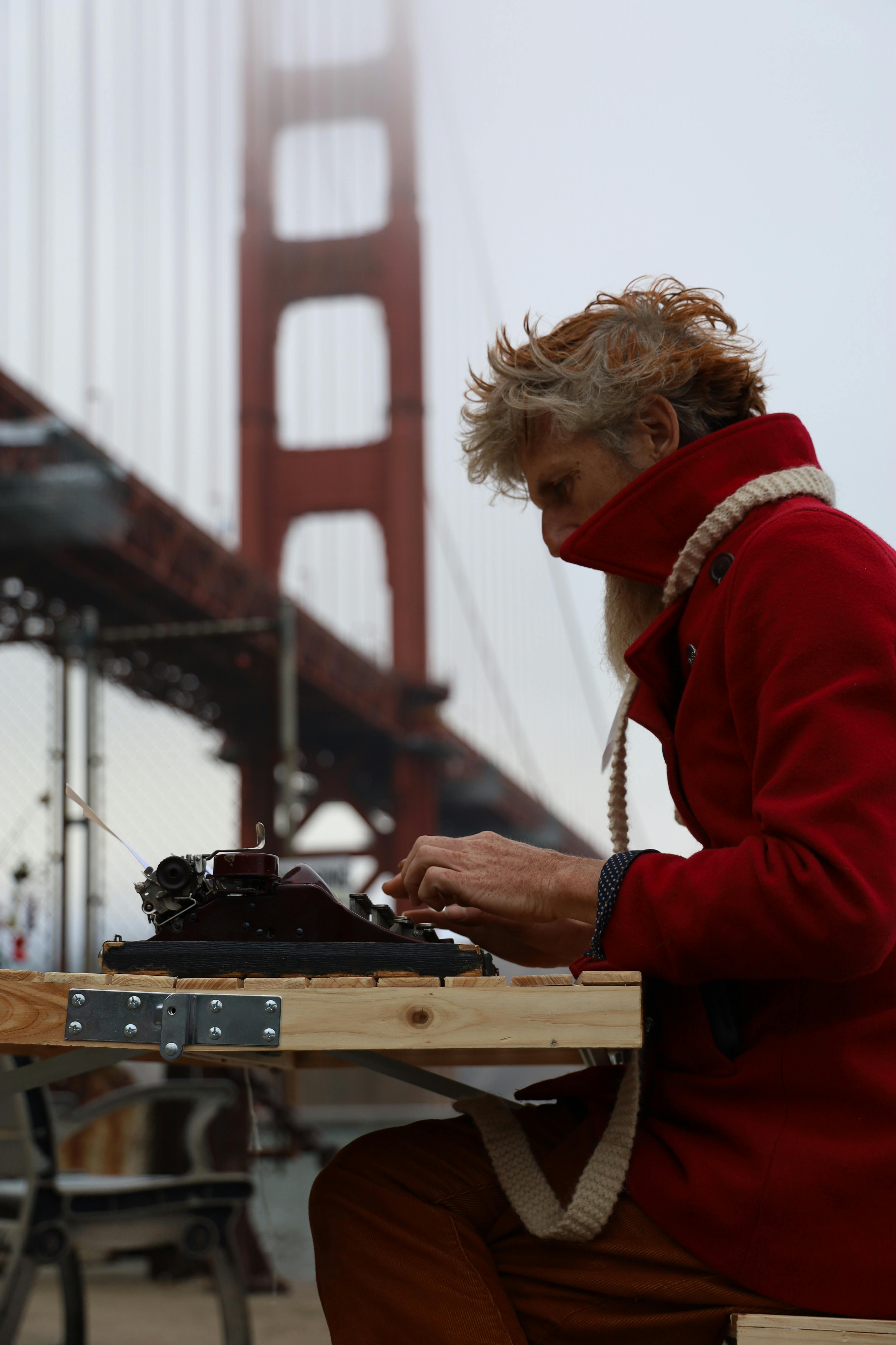 man in red coat sitting near golden gate under fog