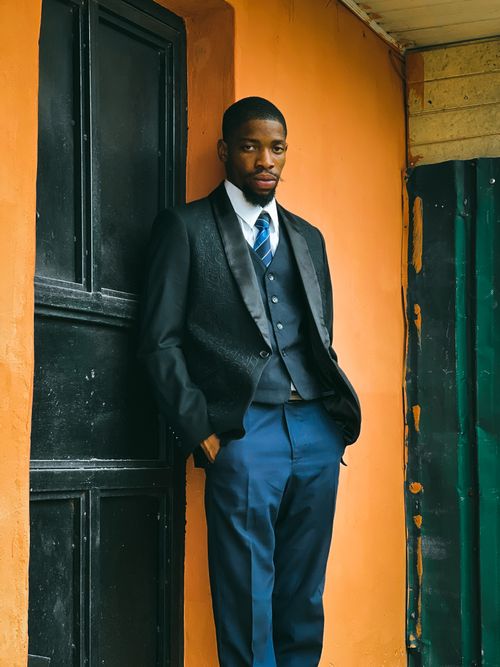 Free A man in formalwear poses confidently against a vibrant orange wall. Stock Photo