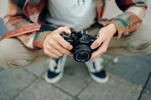 Free A person squatting outside, holding a vintage camera, representing a moment in photography. Stock Photo
