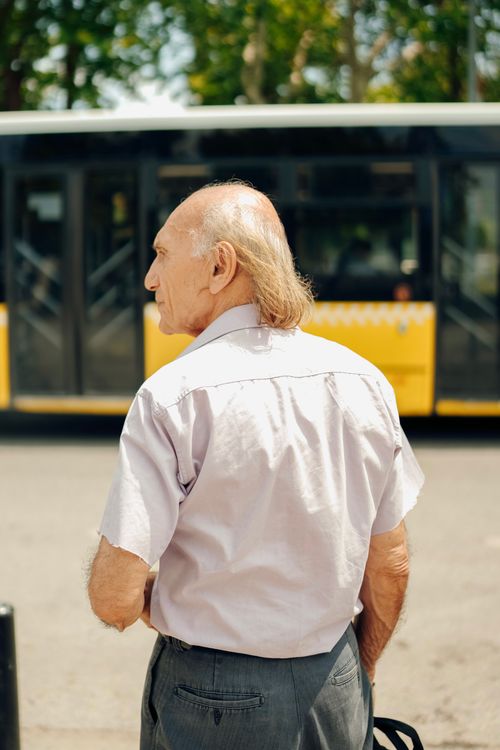 Free An elderly man standing on a city street near a bus with urban surroundings. Stock Photo