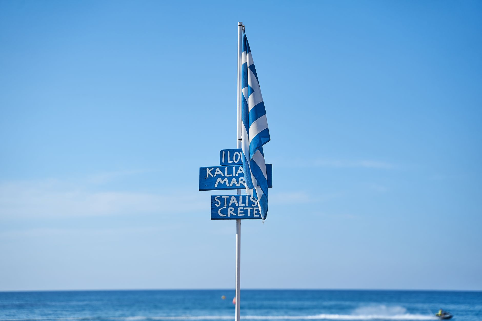 Greek flag flying at a beach in Crete, with blue sky and sea view.