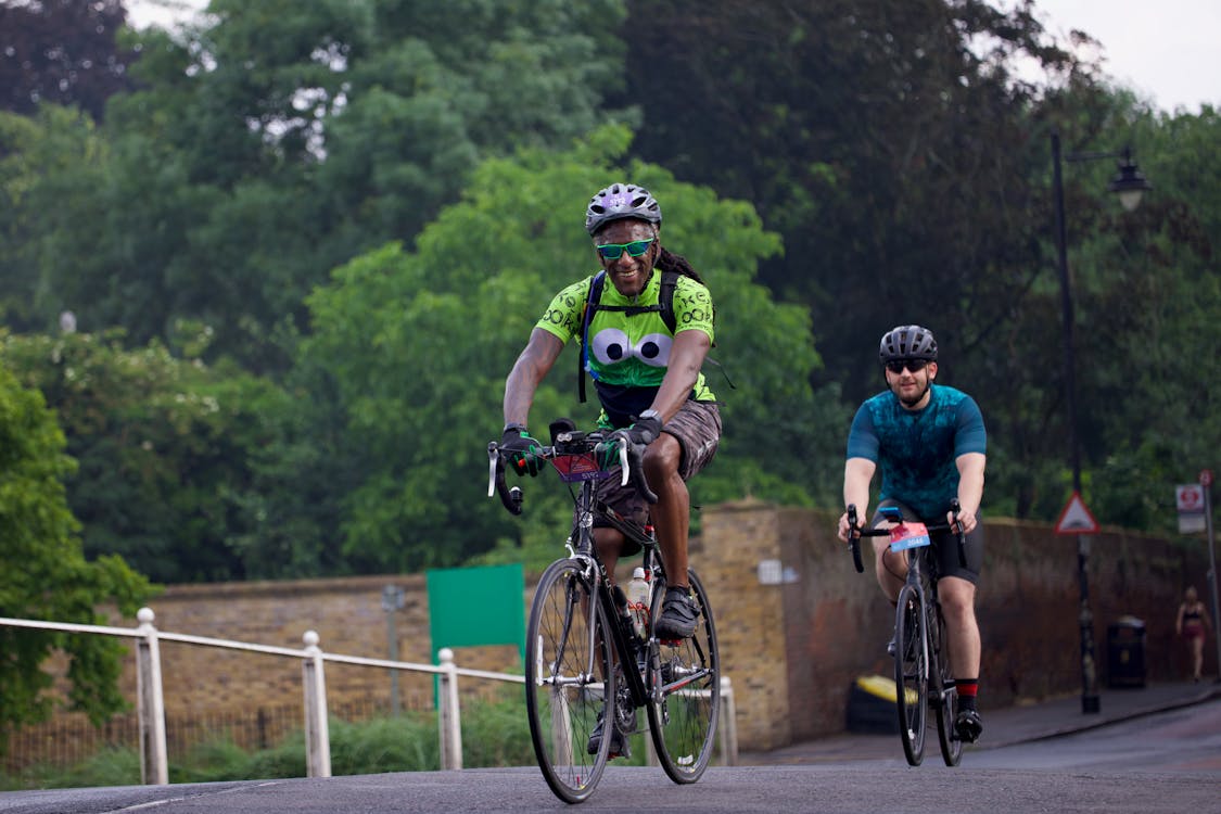 Two people riding bikes on a road with trees · Free Stock Photo