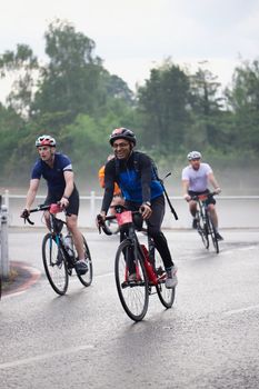 Group of cyclists riding on road during a charity bike event on a misty day.