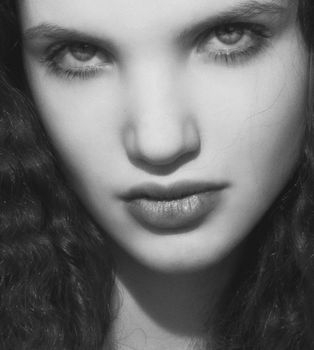 Close-up black and white portrait of a young woman with striking features and curly hair.