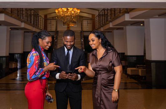 Three colleagues in a formal setting sharing a moment with a smartphone indoors, exuding energy and teamwork.