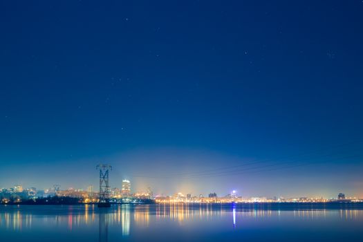 Illuminated cityscape of Dnipro at night with stars reflecting over calm water.