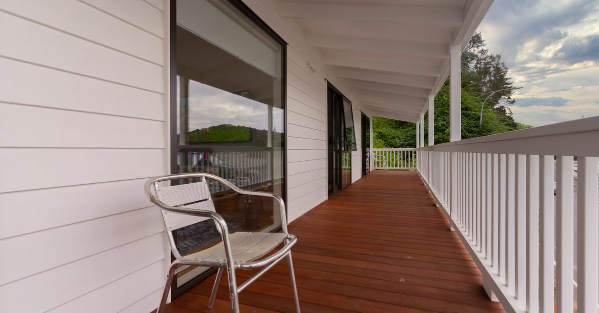 Contemporary wooden porch with metal chair, white facade, outdoor setting.