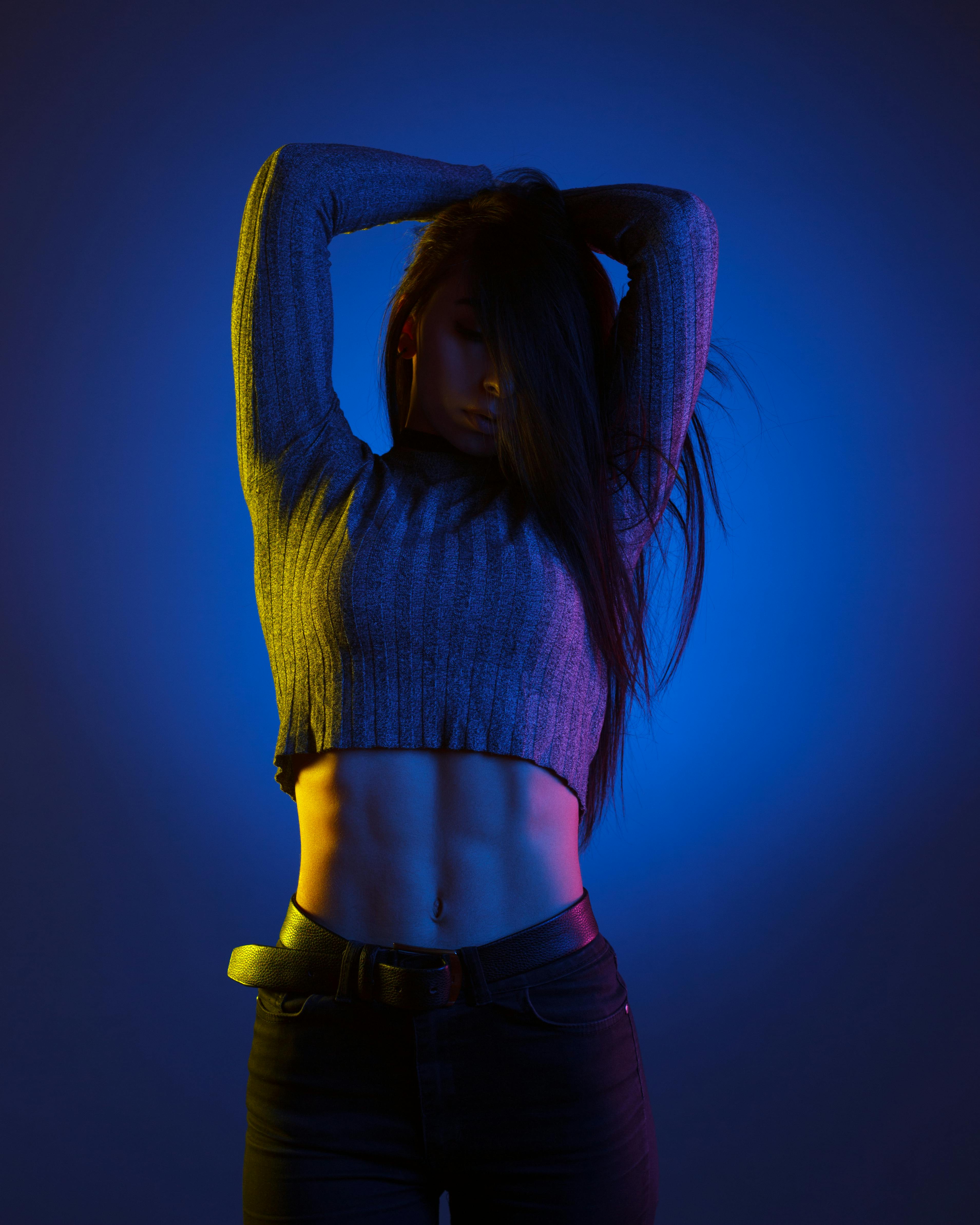 Free Studio shot of a stylish young woman posing with dramatic colored lights, showcasing fashion and fitness. Stock Photo
