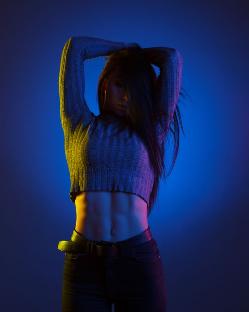 Free Studio shot of a stylish young woman posing with dramatic colored lights, showcasing fashion and fitness. Stock Photo