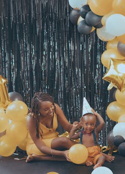 Joyful mother and child celebrate a birthday with colorful balloons and party hats.